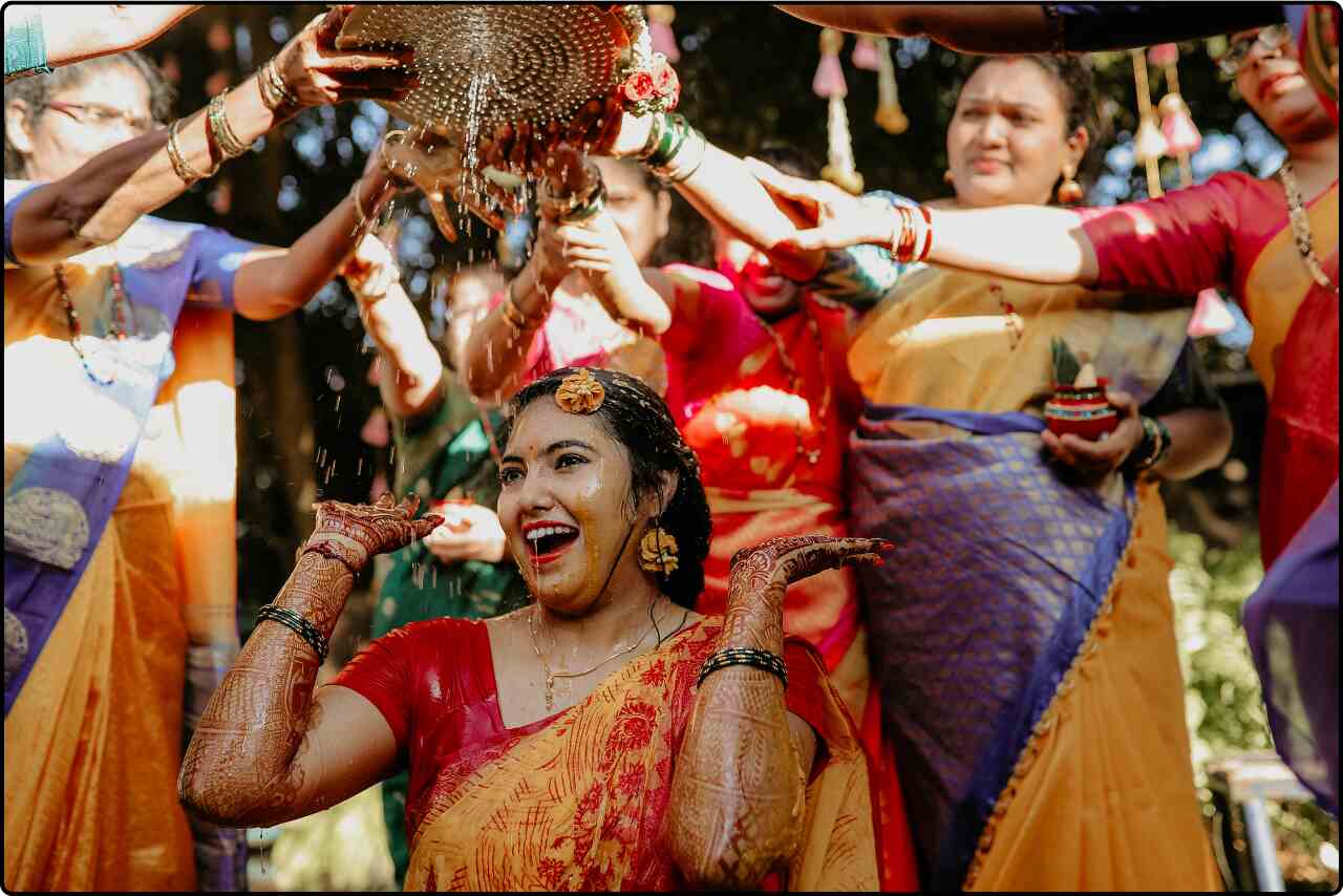 Indian girl smiling as she is covered in turmeric paste during the haldi ceremony at her traditional Indian wedding.